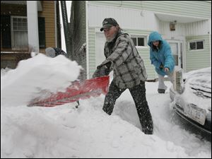 Delton Opfer, center, his 13-year-old granddaughter Vanessa Skouroukos, right, and his 15-year-old grandson John Skouroukos VI, who is almost obscured at back left, clear snow from their sidewalk and around their car in East Toledo.