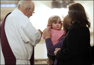 Deacon Tom Carone, left,  gets ready to put ashes on Kady DeWinter, right, held by her grandmother Hope Hutchison.