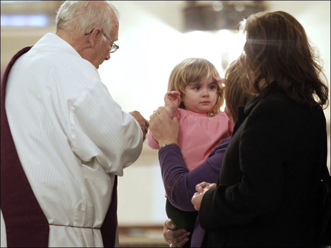 Deacon Tom Carone, left,  gets ready to put ashes on Kady DeWinter, right, held by her grandmother Hope Hutchison.