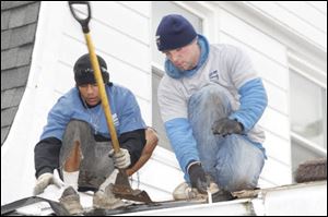 Jonathan Nuzum, left, and Steve McCutchen of Arnold's Home Improvement remove shingles from the Vargases' roof in East Toledo.
