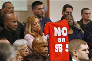 Erika White displays a shirt showing her position on Senate Bill 5 during a news conference Monday at Warren AME Church in Toledo. Her husband, James White, a Toledo firefighter, is at left.