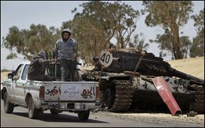 Rebel fighters armed with rocket propelled grenade launchers head back into Ajdabiya, past a previously destroyed pro-Gadhafi forces tank.  