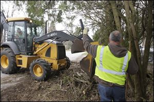 Robert Nash, of Berkey, operating the clam bucket gets some help from Curt Snapp, of Sylvania Township, as they clean up tree debris on a township street. 