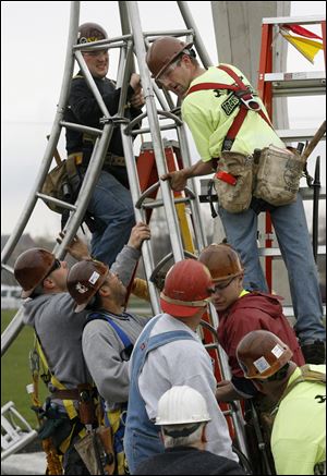 Ironworker apprentices including Rick Hmelewsky, top left, and Stephen Paul, top right, assemble sections of the Veterans’ Glass City Skyway memorial sculpture as they install it in East Toledo Tuesday. The sculpture, designed by Chicago artist Evan Lewis, is a tribute to the men killed and injured during construction of the bridge.