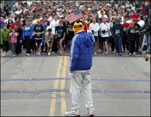 Tom Falvey lofts the flag as runners, at the University of Toledo, await the start of the 5K race. The competitors met winds that gusted to 30 miles an hour.