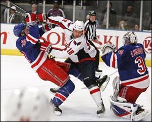 Washington's Marco Sturm fends off New York's Michael Sauer as Rangers goalie Henrik Lundqvist defends.