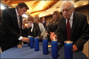 Tom Helberg, left, helps an emotional Clara Rona, a Holocaust survivor, light a candle with Dr. Aron Wajskol, also a Holocaust survivor, at the ceremony. 
