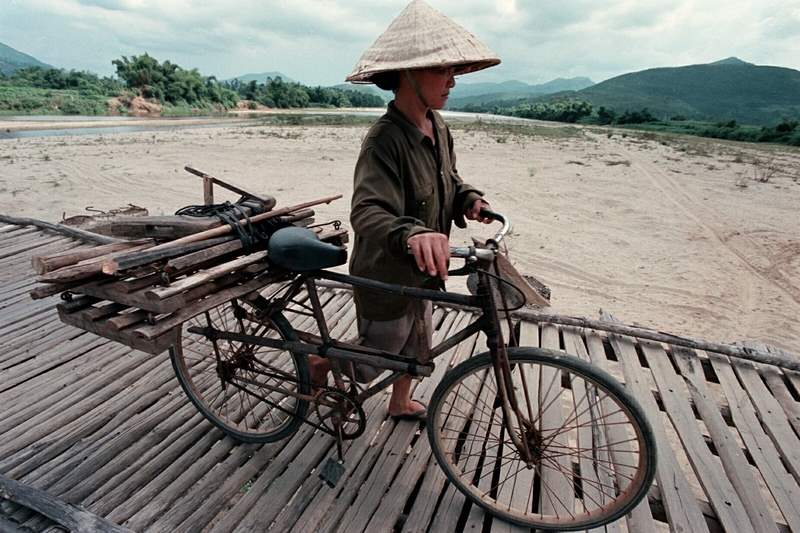 A-woman-pusher-her-bicycle-over-a-hand-made-bridge-stretching-across-the-Song-Ve-River