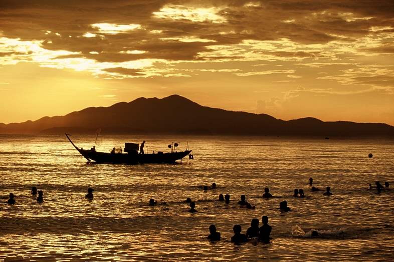 Tourists-swim-in-the-South-China-Sea-near-a-fishing-boat-as-the-sun-rises