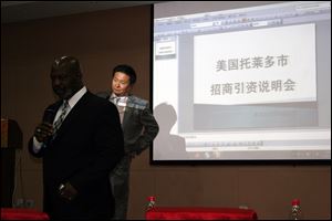 Mayor Mike Bell tells a room of Chinese investors about the merits of Toledo as Simon Guo translates. The screen behind the two men reads: 'City of Toledo Investment Demonstration.'