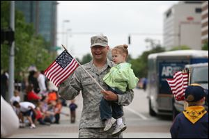 Staff Sgt. Ryan Goodrick carries his year-old daughter, Emma, as he joins other marchers in the parade in downtown Toledo. 