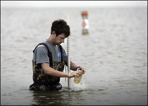 Scott Denham II of the University of Toledo Lake Erie Center takes a sample from Lake Erie at Maumee Bay State Park in Oregon. The sample will go to the lab.