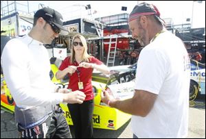 Paul Menard signs his autograph for fan Kevin Griebach, right, as crew member Jody Jennings, center, stands by before practice run.
