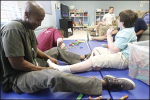 Life coach James Amison, left, helps Ben Smith,right,  who has autism, put on his sock during a new after school program for autistic children at the Self Reliance Center.