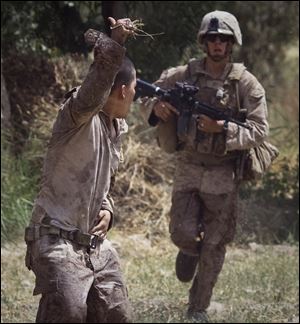 Lance Cpl. Blas Trevino of the 1st Battalion, 5th Marines, left, holds onto the gunshot wound in his belly and gestures toward his troops as he runs to a medevac helicopter from the U.S. Army's Task Force Lift 