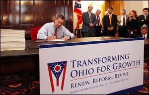 Ohio Gov. John Kasich, left, signs the state budget bill, at the Ohio Statehouse, Thursday.