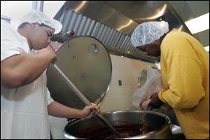 Pierce Baker, 18, stirs sauce as his father, Kyle Baker, adds more ingredients for the startup business Gertie's Premium BBQ Sauce, owned by Kyle Baker and sibling Viveca Crews, both of Toledo, in this 2010 file photo.