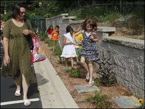 Lizzie Swaile, 7, of Bedford, under the watchful eye of mother Christina Swaile, hops from letter to letter as she travels the path of the Alphabet Garden, where each letter of the alphabet has a flower which begins with that letter at the Children's Garden at the Bedford Public Library in Temperance, Mich.