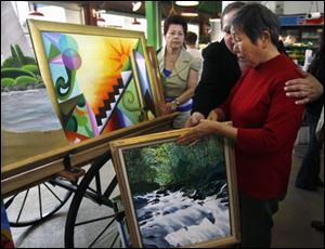 Piedad Gerena, center, helps Wang Huaxian, 73, collect paintings in East Harlem, New York.