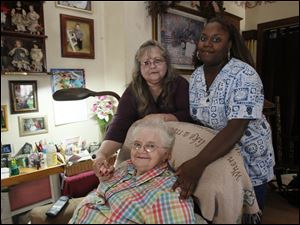 Mary Jackson, 80, seated with her daughter Pam Feichter, standing at left, and caretaker Shantoya Lyons, has lived with her adult daughter and son-in-law Bob since Ms. Jackson's heart attack several years ago. Ms. Lyons, an STNA with Comfort Keepers, works at the family home 25 hours a week through the PASSPORT program.