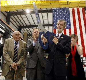 James Viciana, chairman of the board of directors for Ventower Industries, holds up a symbolic pair of scissors after a ribbon cutting ceremony at the dedication of Ventower Industries, Michigan's largest wind power production plant. Behind Mr. Viciana are U.S. Rep. John Dingell (D-Dearborn), left, and Robert Clark, Mayor of Monroe, right.