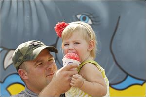 Ben Eisel helps his daughter Lilli Eisel get a big bite out of her snow cone during a refreshing pause to the circus excitement.