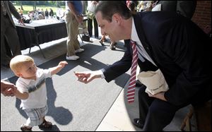 Clark Fry, left, 1, from Fremont, accepts a the newest presidential $1 coin which honors Rutherford B. Hayes from J. Marc Landry, right, plant manager at the United States Mint, at the Hayes Presidential Center.