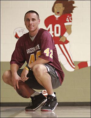 Brian Webster holds a football in front of a painting he made of Pat Tillman in the Pickett Elementary School gymnasium in Queen Creek, Ariz. 