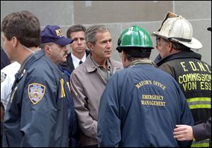 Then President George W. Bush, center, talks to former New York City Fire Commissioner Thomas Van Essen, right, wearing helmet, as New York Police Commissioner Bernard Kerik, left, and former New York City Mayor Rudolph Giuliani, foreground with back to camera, look on during a Sept. 14, 2001, tour of the World Trade Center in New York. 