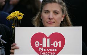 A woman in an area for families of 9-11 victims  holds flowers and a sign that reads 