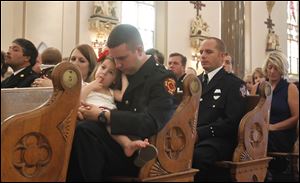 Anthony Santiago, a member of Toledo Fire and Rescue, holds his daughter Kathryn while the names of the fallen are read during the firefighters' Mass at St. Patrick's.  