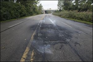 Blackened pavement surrounds a hole where a car exploded on Elm Avenue just east of the I-75 overpass in Monroe.