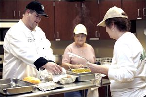 tDoug Corcoran, assisted by Mary Lee Garverick of Sylvania, center, and Luann Takats of Point Place, prepares a God Works meal at Crossroads Community Church.