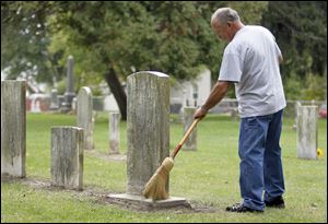 Jim Dusa cleans a grave marker at Wing Cemetery in Petersburg, Mich.
