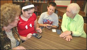 Monroe Middle School seventh graders Rylee Meyer and Nate Goldsmith demonstrate how multifunction calculators work to Barb Liparoto (left) and Peg Morrison (right), both of whom are members of the Monroe High School Class of 1956. 