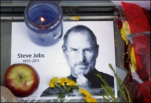 A photograph of Apple co-founder Steve Jobs sits near a candle, an apple and flowers to form a portion of a tribute in front of an Apple store in Boston, Thursday, Oct. 6, 2011.