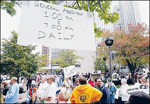 A ‘General Assembly’ sign hangs above rally participants to announce the times for people to come together in Levis Square in downtown Toledo to show their discontent.