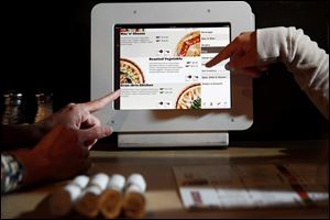 Family members choose from the menu at a restaurant in Torrance, Calif. They flip through a touch screen to view the offerings of pizza, burgers, and salad.