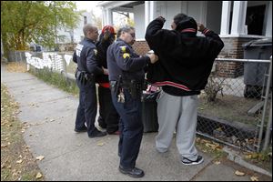Officer Aaron Riter, left, and Sgt. Rick Moreno, right, with the Toledo Gang Task Force, search two members of the gang called 'Lil Head' on Fernwood Ave. in front of the house where Justin Smith was killed last month.