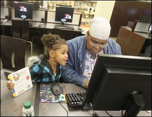 Janice Holmes uses a computer in the newly reopened Kent Branch of the Toledo-Lucas County Public Library as her 3-year-old granddaughter Surrya Silver watches. The branch is in the Old West End.
