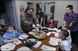 The Johnsons from left: Zachary, 9, dad Jack, Wrennie, 16, Jamyia Brand, 9, John, 11, Jesse, 6, and James Brand, 9, eat dinner in their new Locust St. home in Toledo, Ohio. The Brand family met the Johnsons in the shelter and have remained friends.