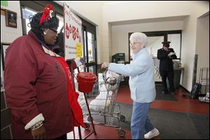 Volunteer Linda Holmes lifts the kettle to make it easier for Collette Box of South Toledo to donate at The Andersons in Maumee. Jerry Hinzman plays Christmas carols in the background.