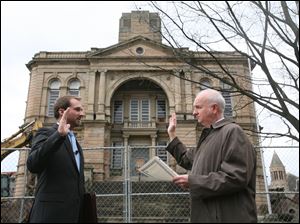 Aaron Montz, 26, left, takes the oath of office from Brent Howard, Tiffin law director, in front of the chain-link fence that surrounds the Seneca County Courthouse. Mr. Montz said Friday he hoped for an order to save the building.