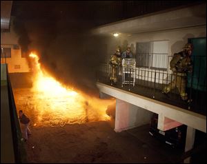 Los Angeles Fire Department firefighters assist a man out of his apartment along with a cage of birds Saturday as multiple cars burn in a carport in the Sun Valley neighborhood of Los Angeles.