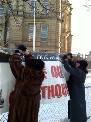 Lenora Livingstone, left, of Tiffin, and Brenda Stultz, of Adams Twp. attach a sign to the fencing around the Seneca County courthouse.