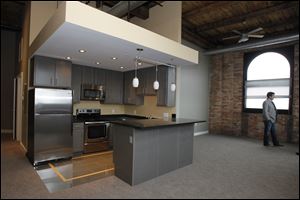 The inside of the Standart Lofts shows the stainless steel appliances and granite countertops, plus the exposed red brick, wood support beams, and high ceilings of bare wooden slats.