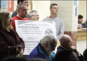 Randy Alcock, left, holds a sign as state Rep. Rick Olson, seated, far right, listens to the board of education meeting in which school cuts were discussed.
