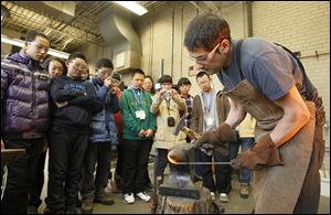Chinese exchange students watch and take photos of a blacksmithing demonstration by Hans Ruebel in the Toledo Museum of Art metalsmithing studio.