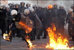 A riot police officers tries to extinguish flames from a petrol bomb thrown by protestors outside the Greek parliament, Athens on Sunday. Tens of thousands of protesters gathered in the square outside Parliament as a parliamentary debate began, with more arriving constantly. As the crowds grew, a few hundred anarchists started to throw bottles and firebombs at police, who responded with tear gas and stun grenades. (AP Photo/Thanassis Stavrakis)