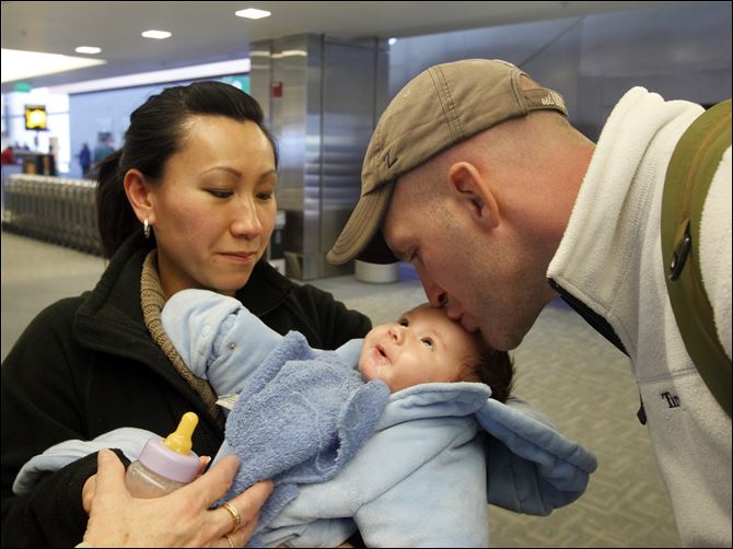 Kevin Johnson, 29, a 2000 Springfield High School alumnus with his wife Hanh Nguyen, kisses his 3-month-old son Jaxon, at Detroit Metro Airport, Feb. 14. 